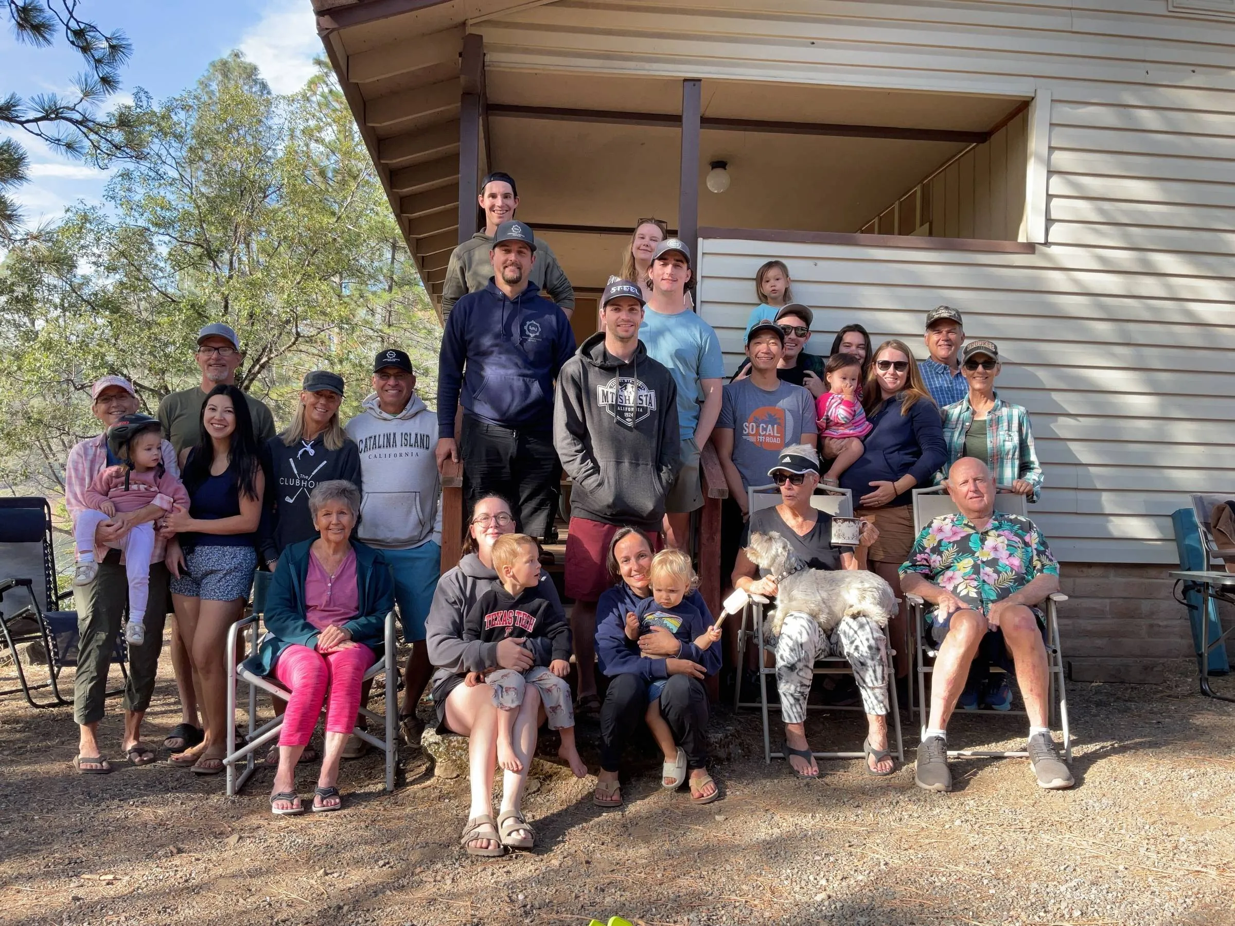 Ben’s extended family, more than twenty people spanning four generations plus a dog, gathered on and around the porch steps of a cabin in the pines