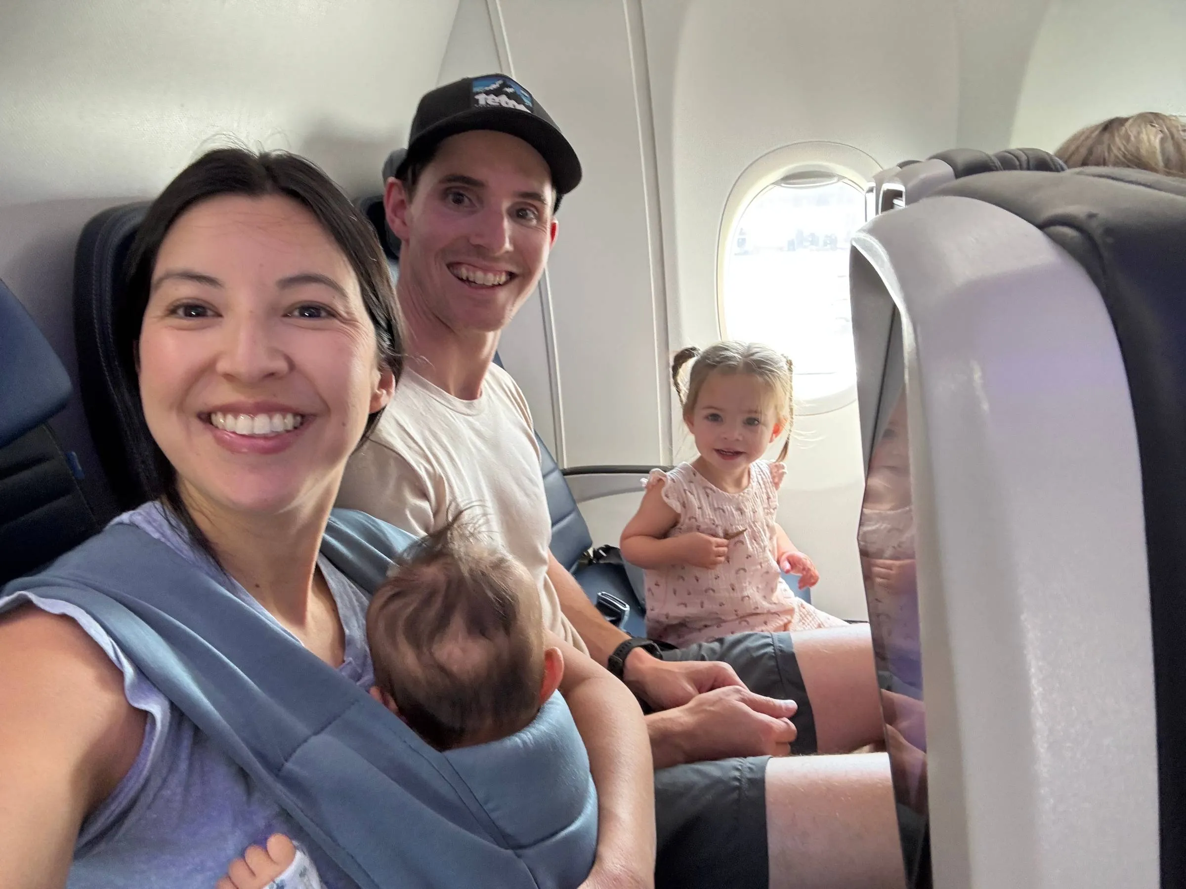 Ben, his wife, their toddler daughter and baby daughter smiling for a selfie in an airplane cabin