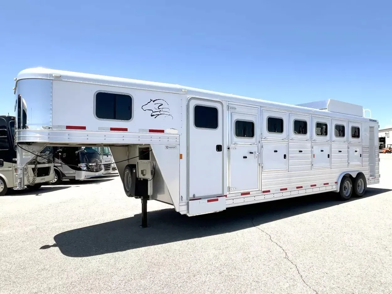 A long white gooseneck horse trailer with living quarters and six stall doors parked on a lot under a clear blue sky