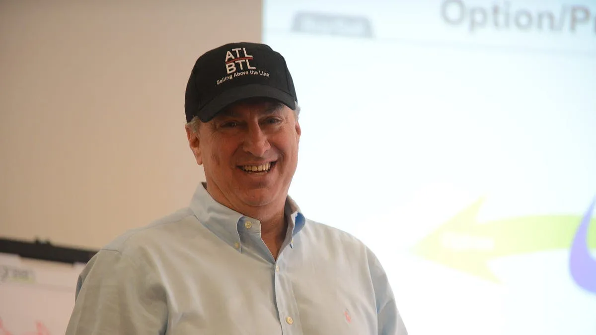 Skip Miller smiling while teaching a sales boot camp, wearing a black cap reading “ATL BTL - Selling Above the Line”
