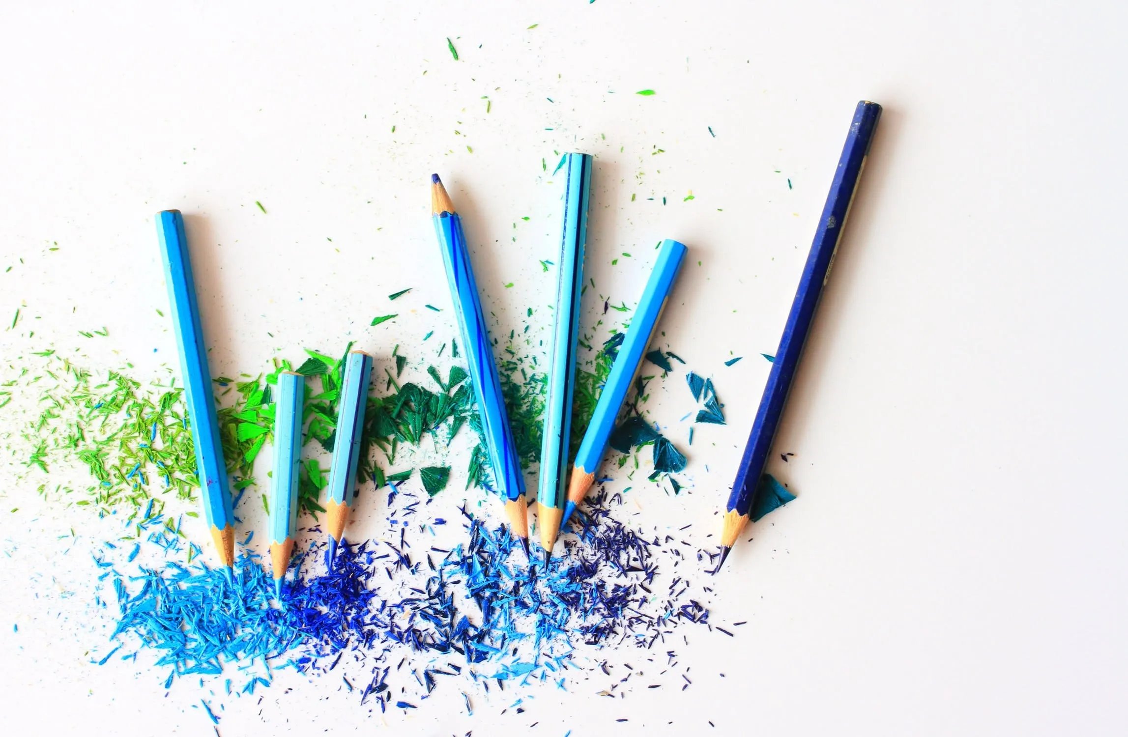 Blue and green colored pencils with shavings arranged on a white surface