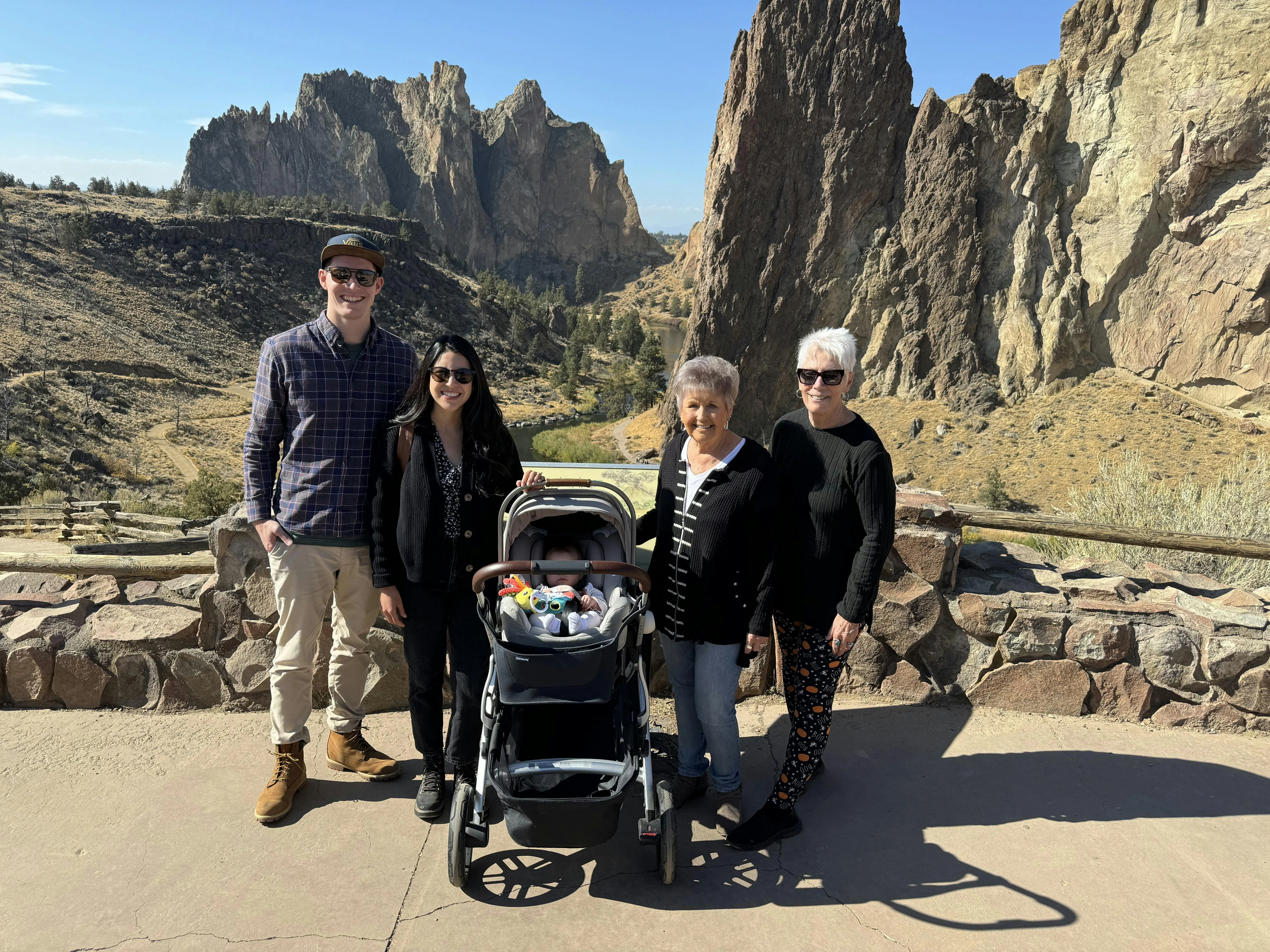 A family of four adults with a baby in a stroller posing in front of the towering rock formations at Smith Rock