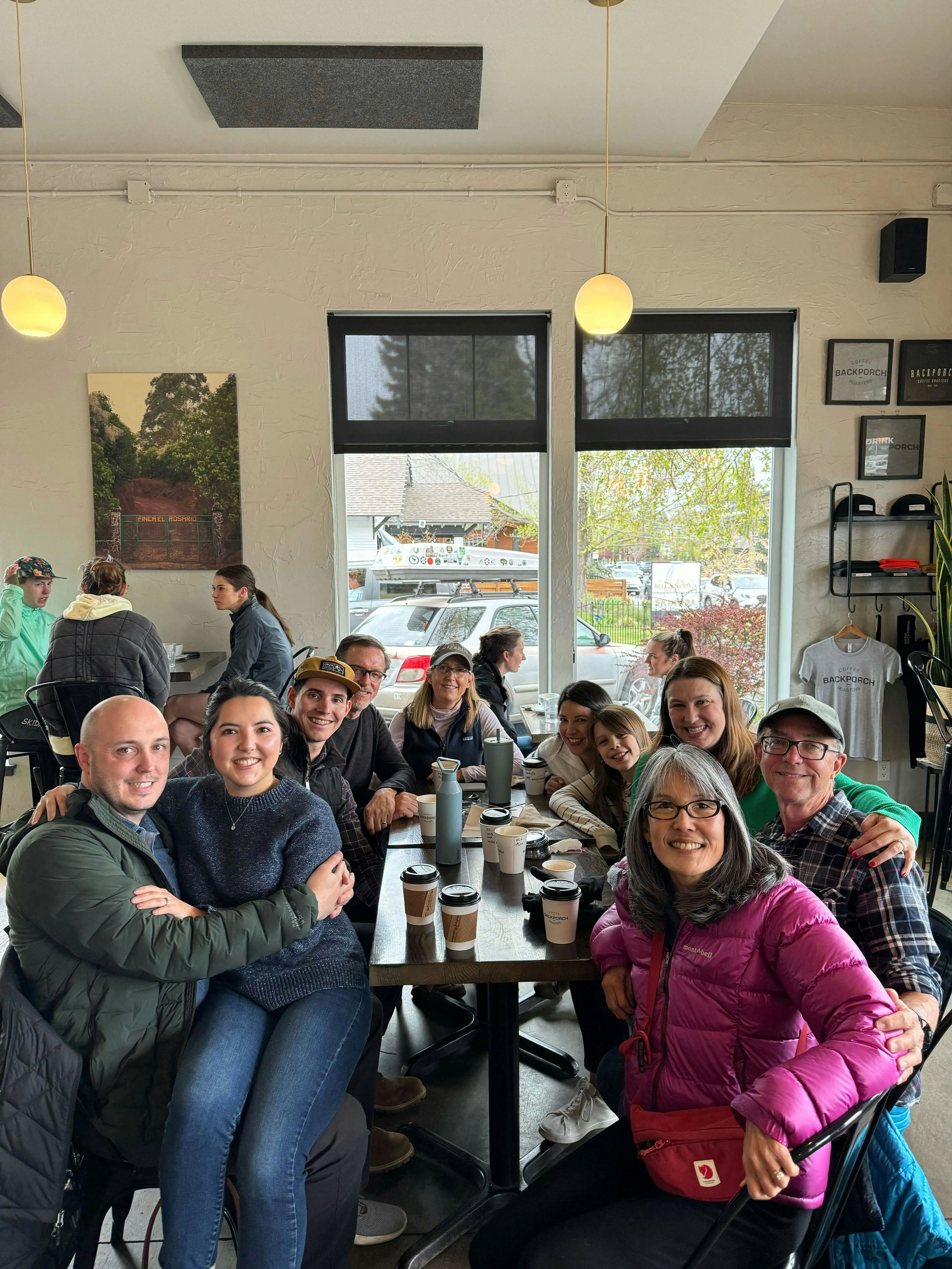 Large family group smiling together around a table at a coffee shop, holding to-go coffee cups