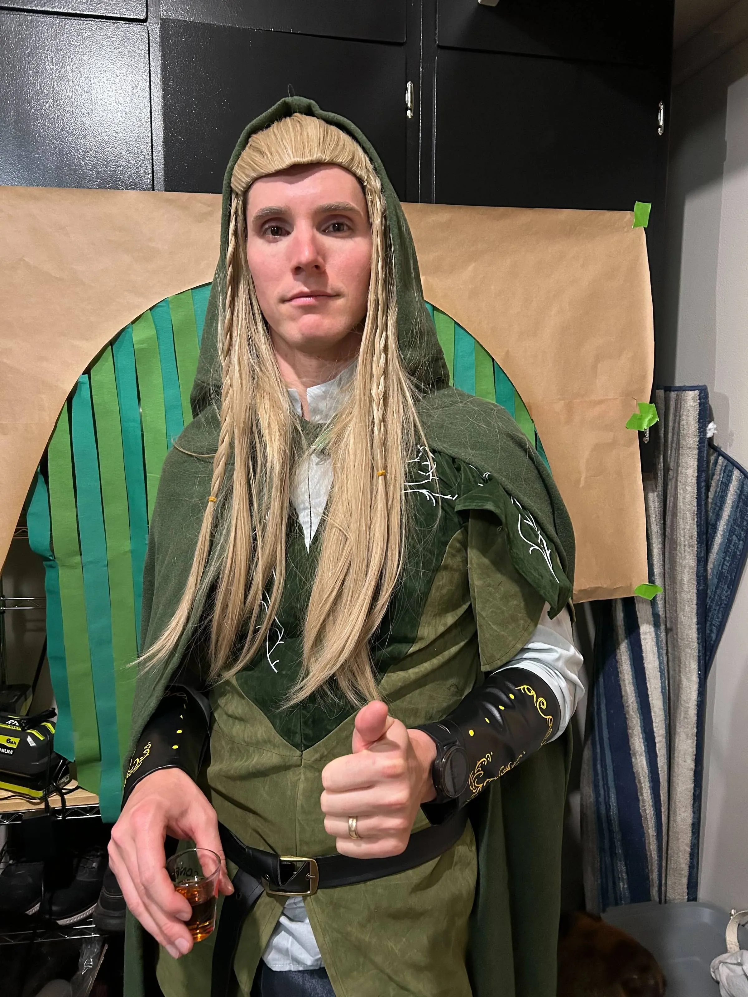 Ben dressed as Legolas in a green elf costume and long blonde wig, giving a thumbs up while holding a shot glass