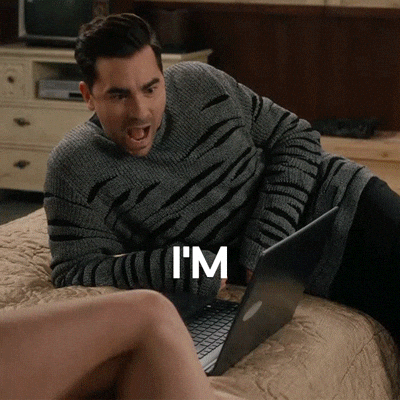 David Rose from Schitt’s Creek lying on a bed with a laptop, saying “I’m obsessed with this”