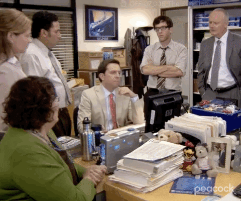 GIF from The Office of coworkers gathered awkwardly around a desk