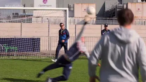 Animated clip of a goalkeeper diving to make a save as a ball flies toward the net on a grass soccer pitch