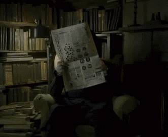Animated GIF of a person reading a large newspaper in a dark, book-filled study