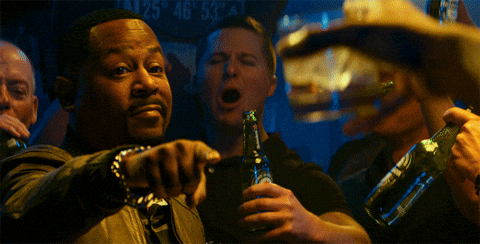 A group of men in a dimly lit bar clinking beer bottles together in a celebratory toast