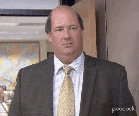 Kevin from The Office in a suit glancing around uncertainly in a reaction GIF